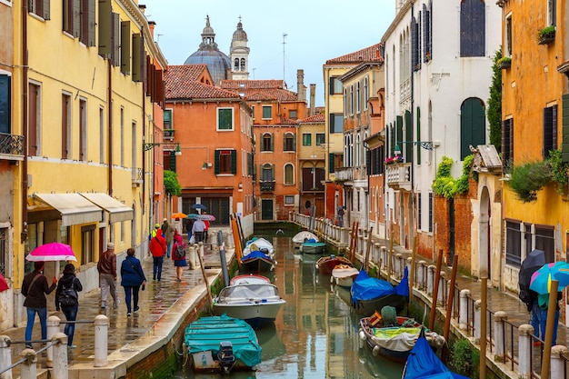 Touristen gehen an einem regnerischen Tag Italien unter Sonnenschirmen entlang eines venezianischen Kanals