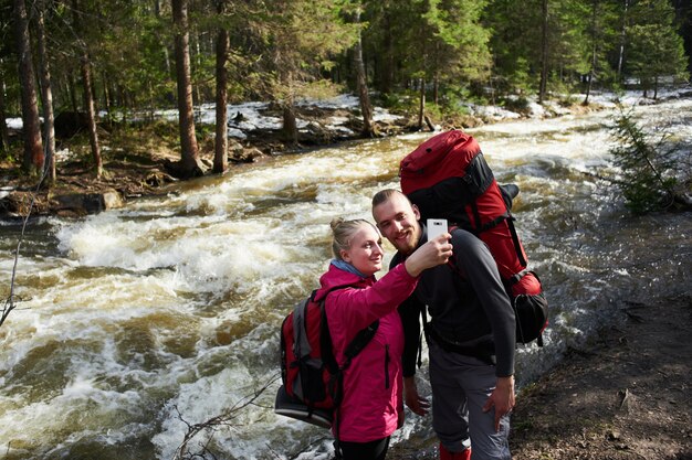 Touristen sind ein Mann und ein Mädchen, die ein Selfie vor dem Hintergrund eines Bergbachs und eines Waldes machen