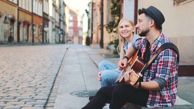 Touristen sitzen auf dem Bürgersteig, spielen Gitarre und ruhen sich aus