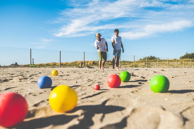 Touristen spielen ein aktives Spiel, Petanque, an einem Sandstrand am Meer. Eine Gruppe junger Leute spielt Boule im Freien während eines Strandurlaubs. Bälle auf dem Boden.