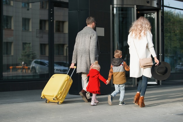 Touristenfamilie, Vater, Mutter, Tochter und Sohn mit gelbem Koffer betreten das Hotel.