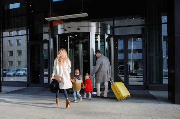 Touristenfamilie, Vater, Mutter, Tochter und Sohn mit gelbem Koffer betreten das Hotel.