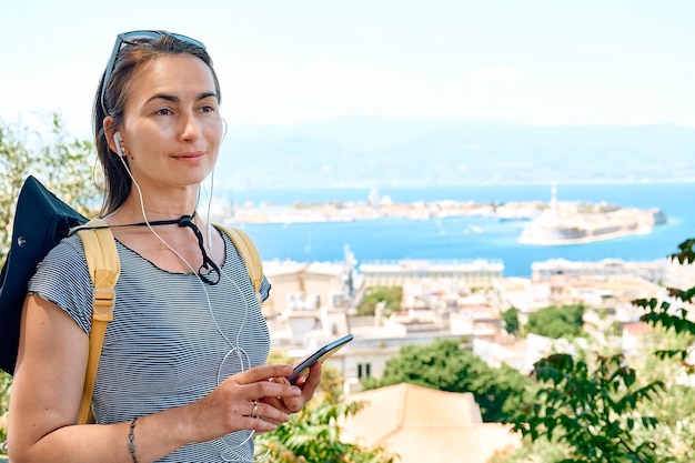 Touristenfrau beobachtet Gebäude in der Nähe des Panoramablicks von Messina und hört sich den Audioguide an