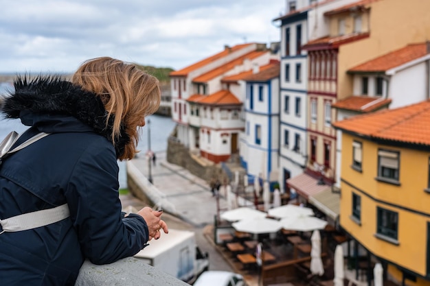 Touristenfrau, die sich aus einem Straßenbalkon herauslehnt und die Aussicht auf das Fischerdorf Cudillero Asturias betrachtet