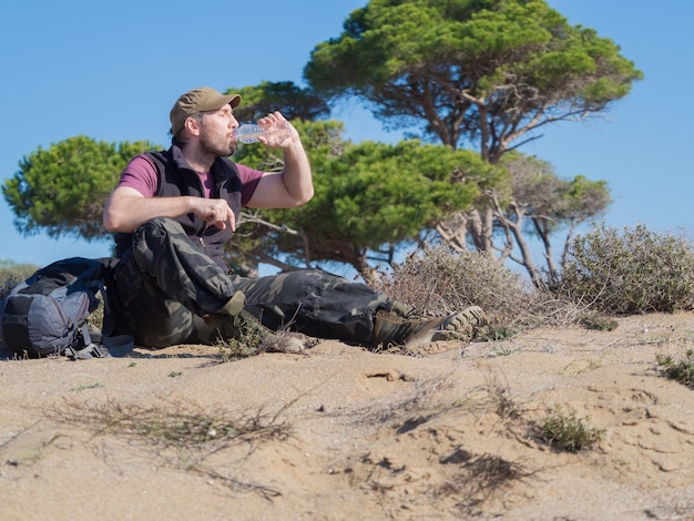 Touristenmann trinkt Wasser aus der Plastikflasche während der Pause bei einem Wüstenspaziergang