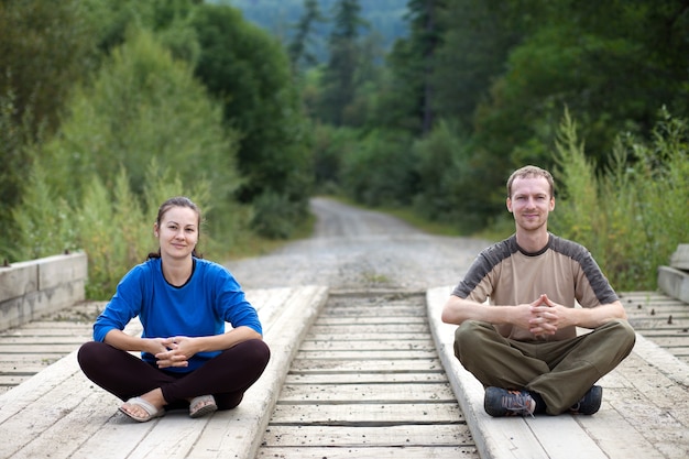 Foto touristenpaar sitzt auf einer holzbrücke mit wald herum