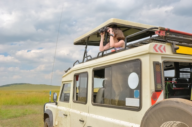 Touristin auf Safari in Afrika, Reisen in Kenia, Wildtiere in der Savanne mit einem Fernglas beobachten