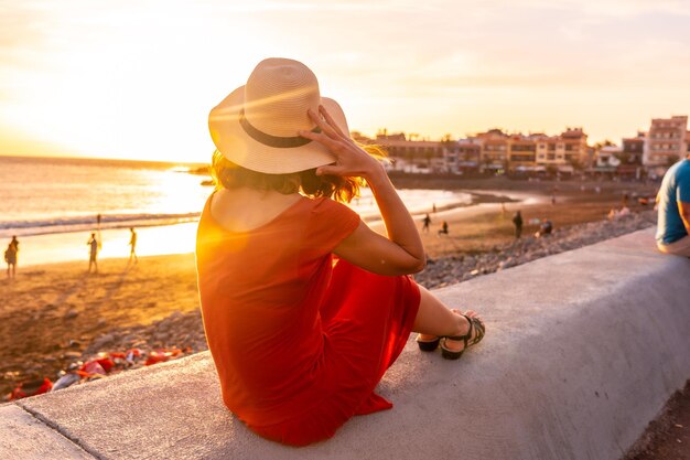 Touristin bei Sonnenuntergang mit rotem Kleid im Urlaub am Strand der Stadt Valle Gran Rey auf den Kanarischen Inseln La Gomera