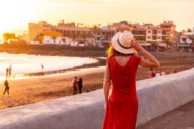 Touristin bei Sonnenuntergang mit rotem Kleid im Urlaub am Strand des Dorfes Valle Gran Rey auf den Kanarischen Inseln La Gomera. Spaziergang am Strand entlang