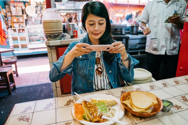 Touristin, die den traditionellen Taco auf dem Markt probiert und zuerst das Telefon essen lässt. unabhängiges reisen des jungen mädchens in den usa. Reisende, die das mexikanische Essen auf ihrer Urlaubsreise aufzeichnet.