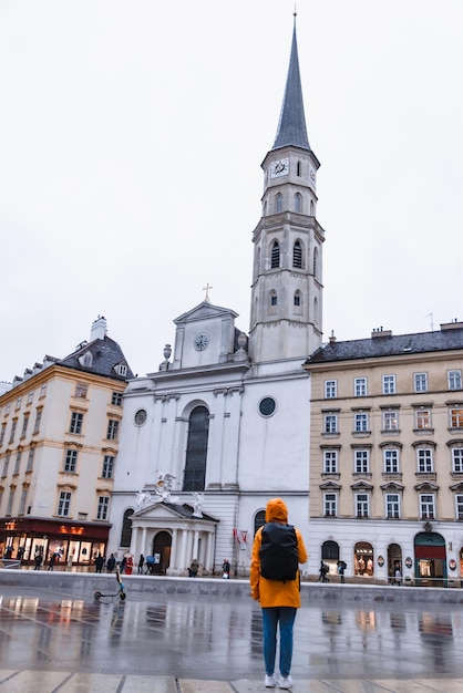 Touristin im gelben Regenmantel mit Rucksack, der die St.-Michaels-Kirche betrachtet