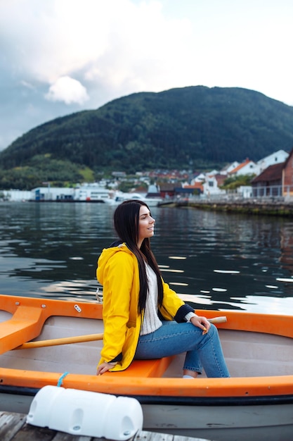 Touristin in gelber Jacke sitzt und posiert in einem Boot vor dem Hintergrund der Berge