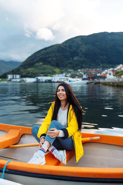 Touristin in gelber Jacke sitzt und posiert in einem Boot vor dem Hintergrund der Berge