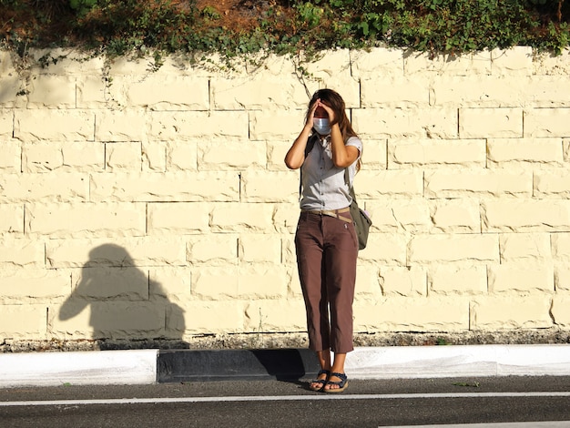 Touristin in medizinischer Maske steht am Straßenrand und bedeckt ihr Gesicht vor der Sonne