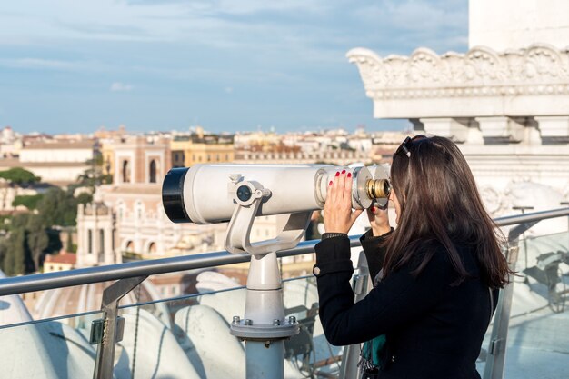 Touristin schaut von einem hohen Punkt aus durch ein Fernglas auf die Stadt Rom