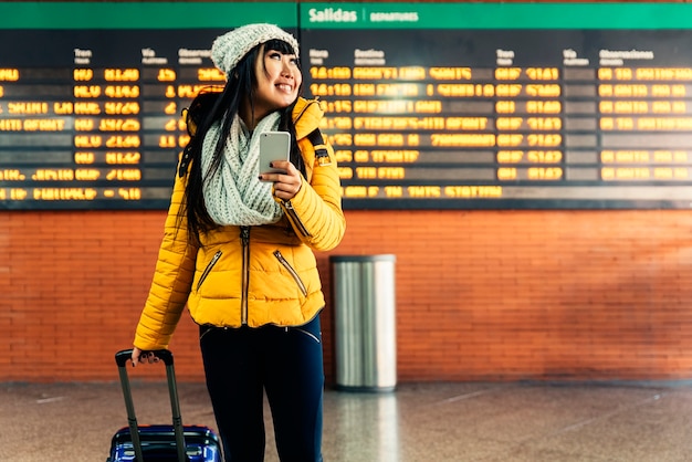 Touristische asiatische Frau mit Handy im Bahnhof. Tourismus-Konzept.