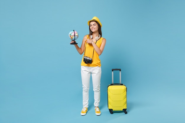 Touristische Frau des Reisenden in gelber Freizeitkleidung, Hut mit Kofferfotokamera auf Blau