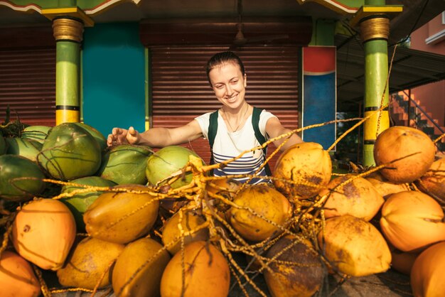 Touristische Frau, die den lokalen asiatischen Markt erkundet und glücklich ist, reife Kokosnüsse zu sehen