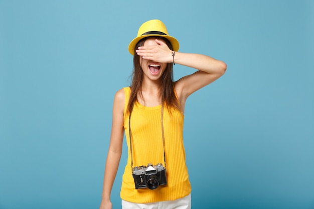 Touristische Frau in gelber Sommerkleidung und Hut mit Fotokamera auf Blau