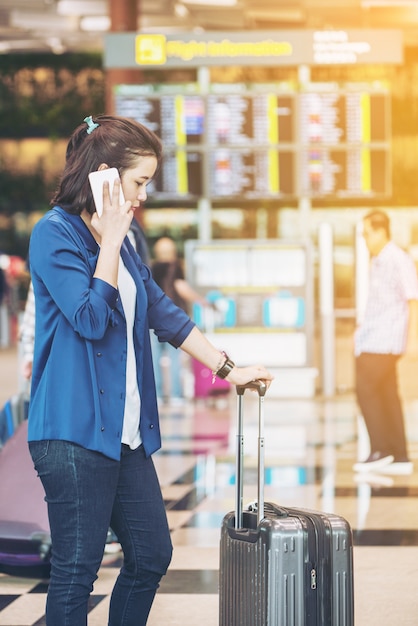 Touristische Frau mit Gepäck im Flughafen. Glücklicher junger Reisender mit Handy.