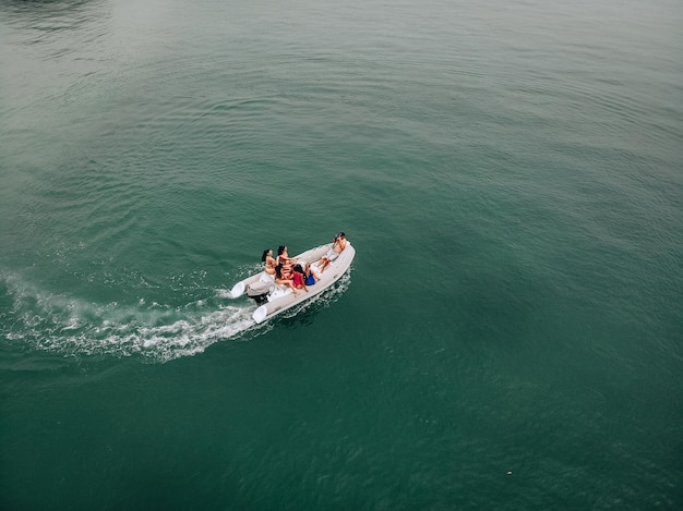 Touristische Luftaufnahmen auf dem offenen, klaren, türkisfarbenen Meer. Ein junger Mann führt eine Fotosession für junge hübsche Mädchen in Badeanzügen auf einem weißen Motorboot durch. Gruppe posiert für die Kamera.