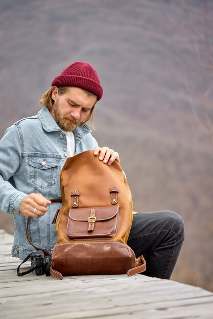 Touristischer Mann, der ledernen braunen Rucksack während der Wanderung in den Bergen öffnet, Seitenansicht