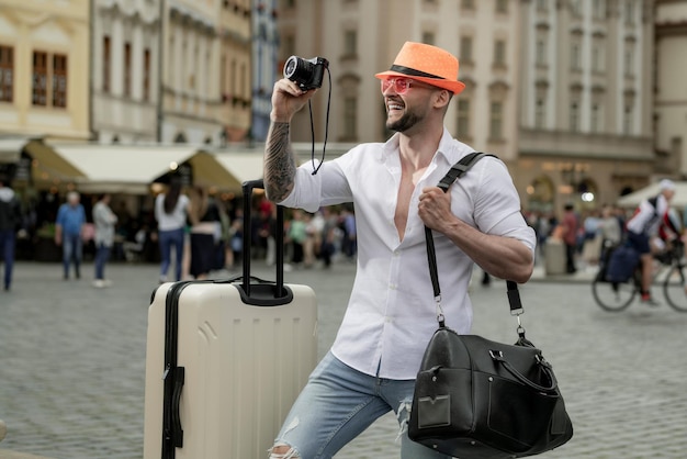 Foto touristischer mann in mode, hut, jeans und sonnenbrille mit koffer, der auf straßenfoto von mannreisen geht