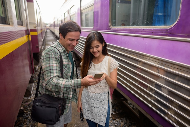 Touristischer Mann und junge asiatische Frau, die Telefon am Bahnhof verwenden
