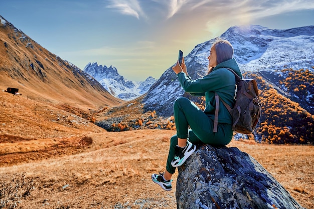 Touristischer Reisender, der allein auf einer felsigen Spitze sitzt und ein Foto mit der Telefonkamera der Bergtallandschaft in Juta, Georgia, macht