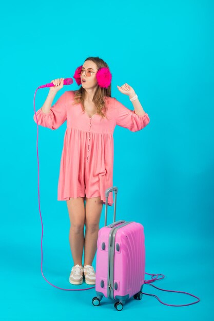 touristisches mädchen in einem rosa kleid mit einem rosa mikrofon auf einem blauen hintergrund, der einen rosa koffer hält