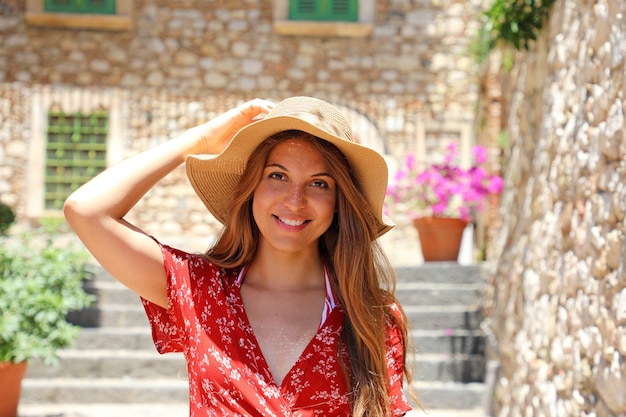 Touristisches Mädchen mit Hut und rotem Kleid, das auf gemütlicher italienischer Straße in Taormina, Sizilien aufwirft