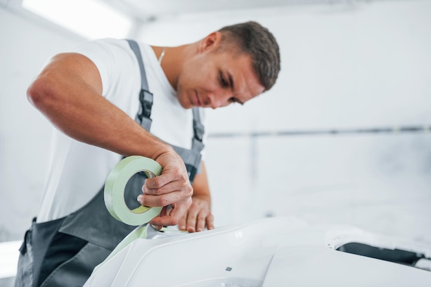 Trabaja con el capó del automóvil Reparador de automóviles caucásicos en uniforme en el garaje