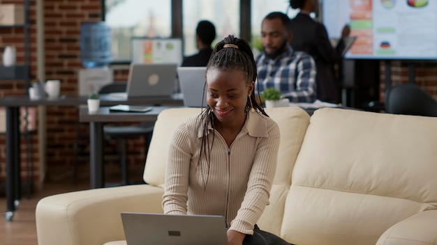 Trabajador afroamericano analizando gráficos comerciales y estadísticas financieras en una computadora portátil para planificar el desarrollo. Empleada que crea una presentación de marketing en línea en una computadora en la oficina.