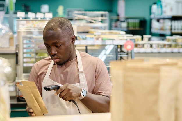 Trabajador afroamericano escaneando códigos de barras de productos con escáner durante su trabajo en el supermercado