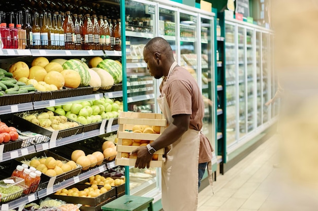 Trabajador afroamericano de supermercado llevando frutas frescas a la venta