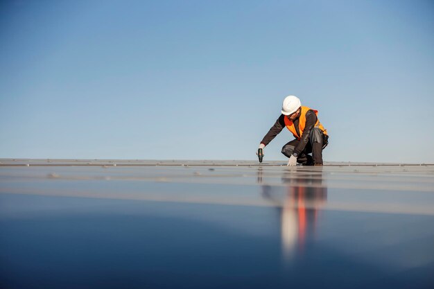 Un trabajador agachado en la azotea e instalando paneles solares