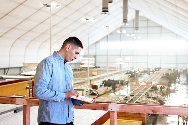 Trabajador agrícola automatizado industrial con computadora portátil en el fondo de la producción de leche de vaca y carne de res