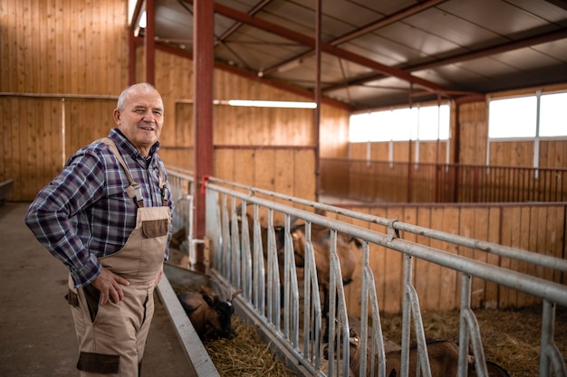 Trabajador agrícola de pie junto a los animales domésticos y mirando a la cámara