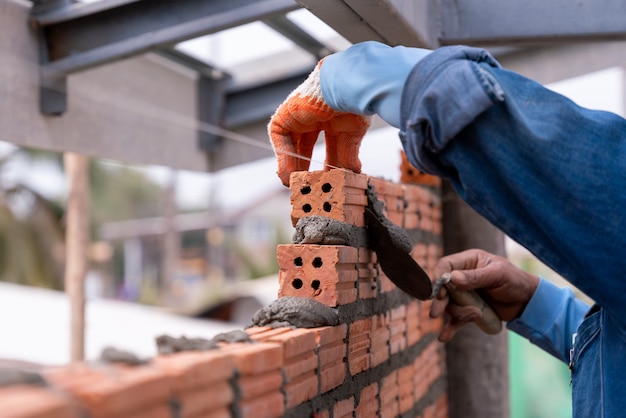 Foto trabajador de albañil instalando mampostería de ladrillo en la pared con espátula de paleta en el sitio de construcción.