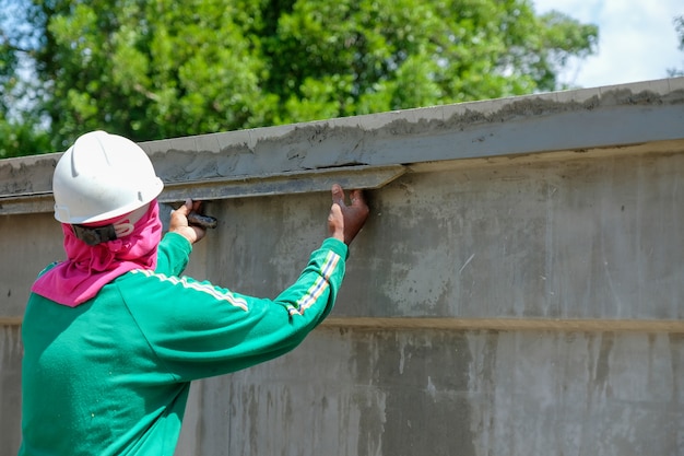 Un trabajador de albañilería que enyesa el cemento en la pared de cemento en el tiempo caliente en el emplazamiento de la obra.