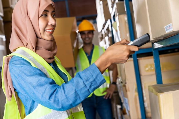 Foto trabajador de almacén femenino musulmán islam asiático haciendo inventario con escáner de código de barras