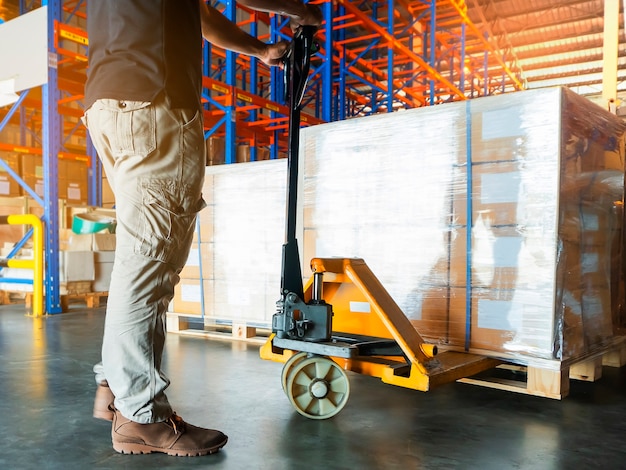 Trabajador de almacén con transpaleta manual descarga carga de envío en el almacén de almacenamiento.