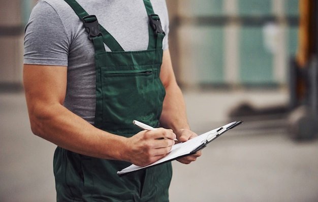 Trabajador de almacenamiento en uniforme de color verde y bloc de notas en manos comprueba la producción.