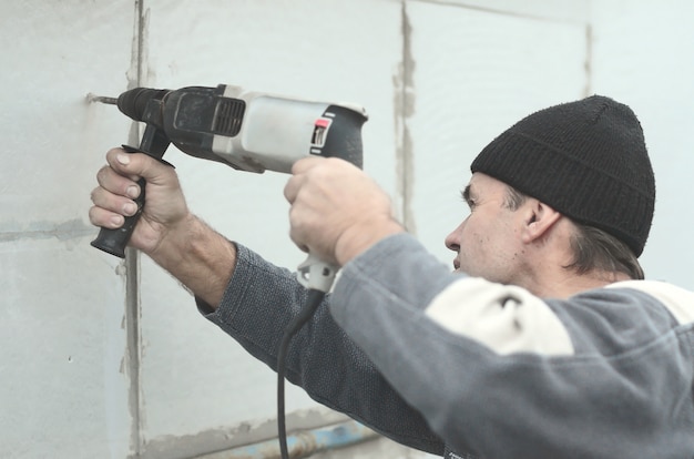 Foto un trabajador anciano perfora un agujero en una pared de espuma de poliestireno