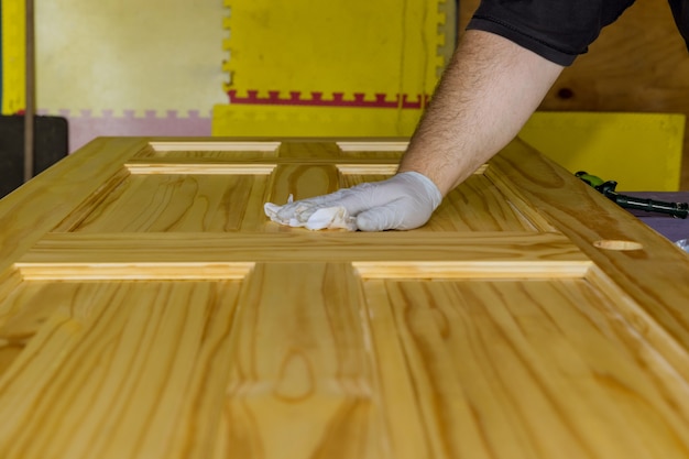 Trabajador aplicando barniz protector en una puerta de madera con pincel