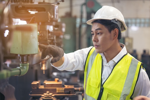 Trabajador asiático con un casco revisa la maquinaria en una fábrica.