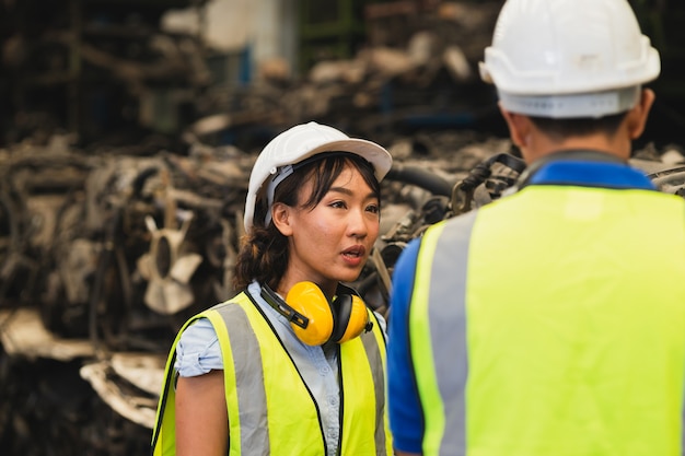 Trabajador asiático del ingeniero que trabaja las mujeres que trabajan junto con el hombre joven en el lugar de trabajo de la industria pesada waring casco traje de seguridad