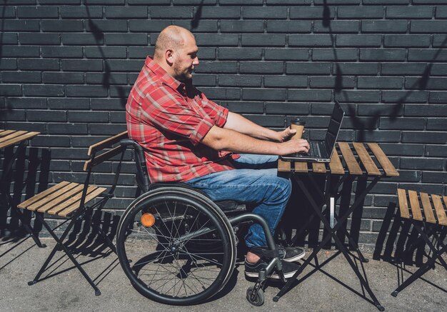 Trabajador autónomo con discapacidad física que usa silla de ruedas y trabaja en el café de la calle.