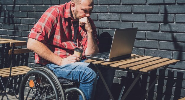 Trabajador autónomo con discapacidad física que usa silla de ruedas y trabaja en el café de la calle.