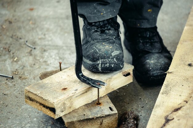 Trabajador con botas ásperas saca clavos de tablones de madera Construcción y reparación